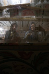 تصویر دو بافنده هنرمند را در حال پودگذاری در کارگاه فرش فراهان را نشان میدهد